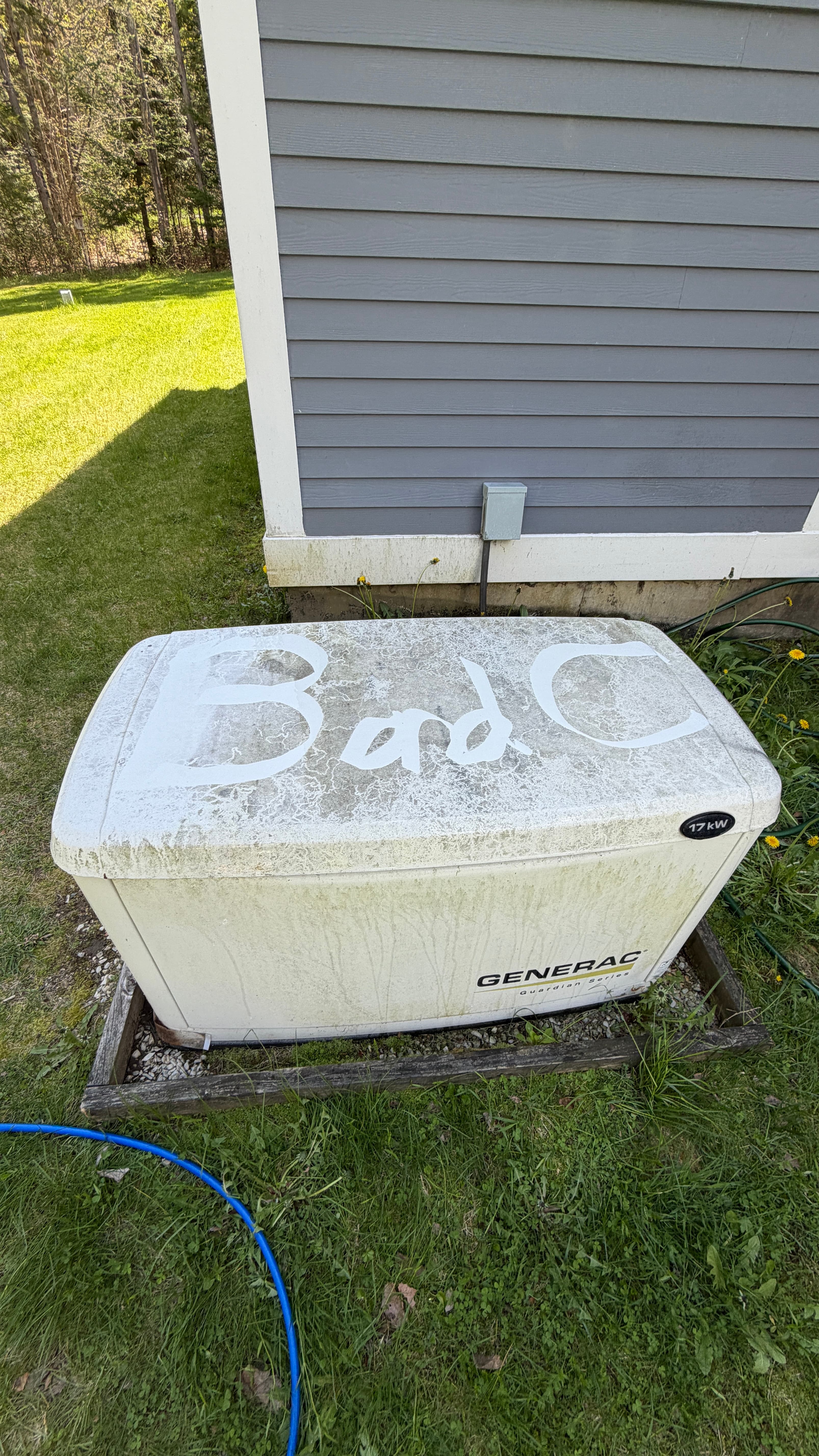 Weathered Generac generator with 'Bad C' written on top, sitting in a grassy yard.