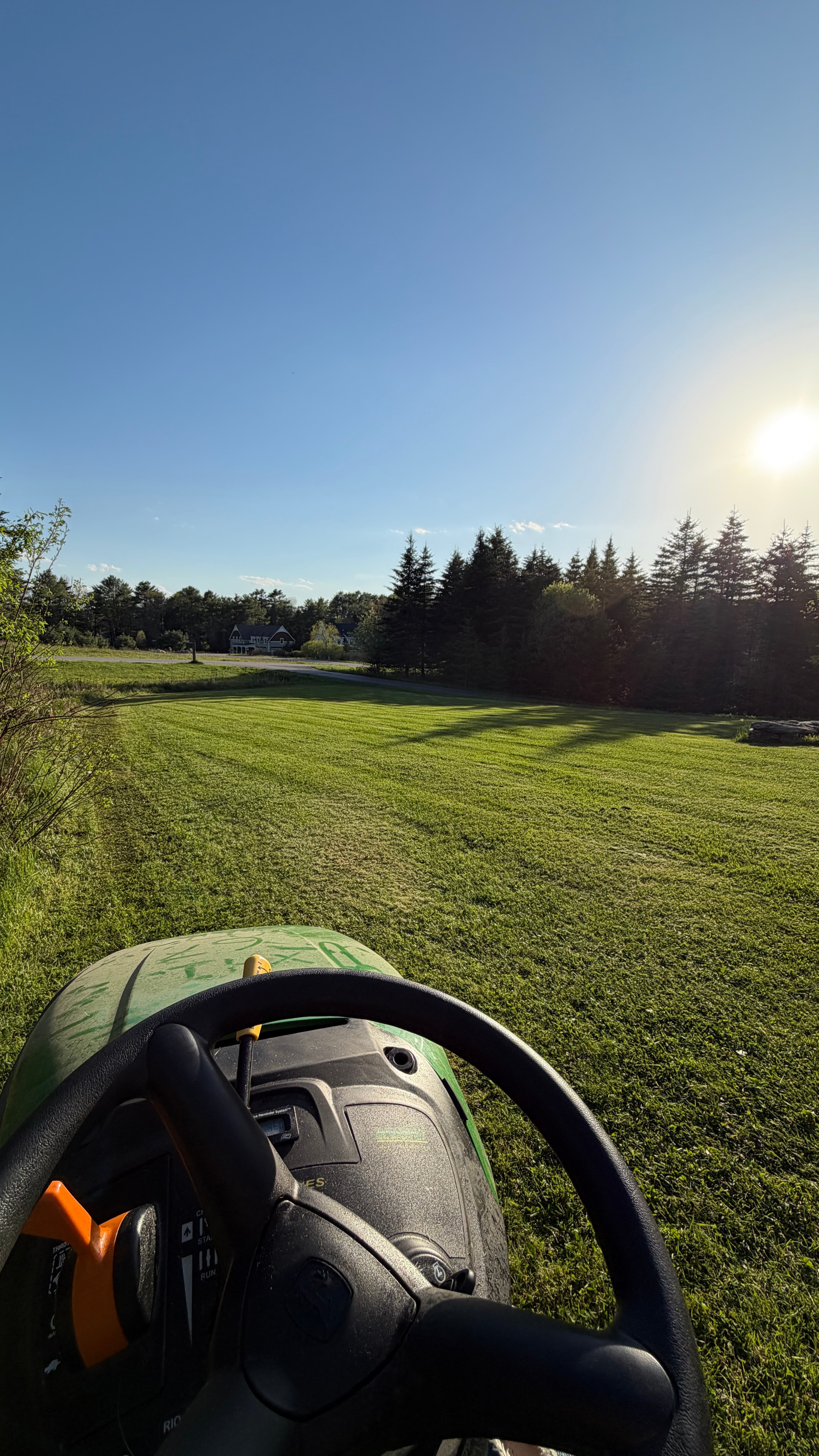 View from a lawn mower overlooking a vast green field under a bright sun.