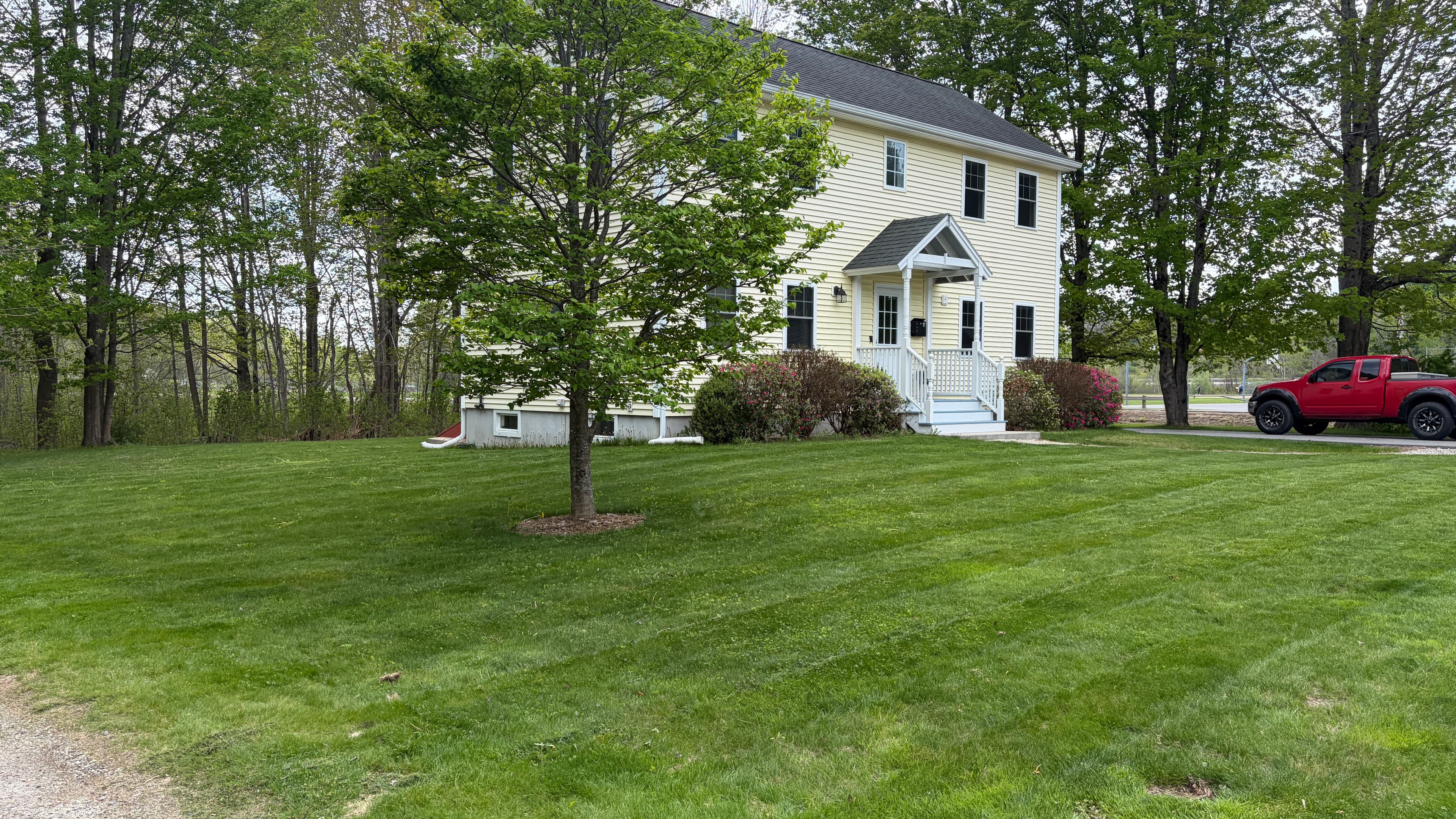 Yellow two-story house with white trim on a green lawn, featuring a red pickup truck.