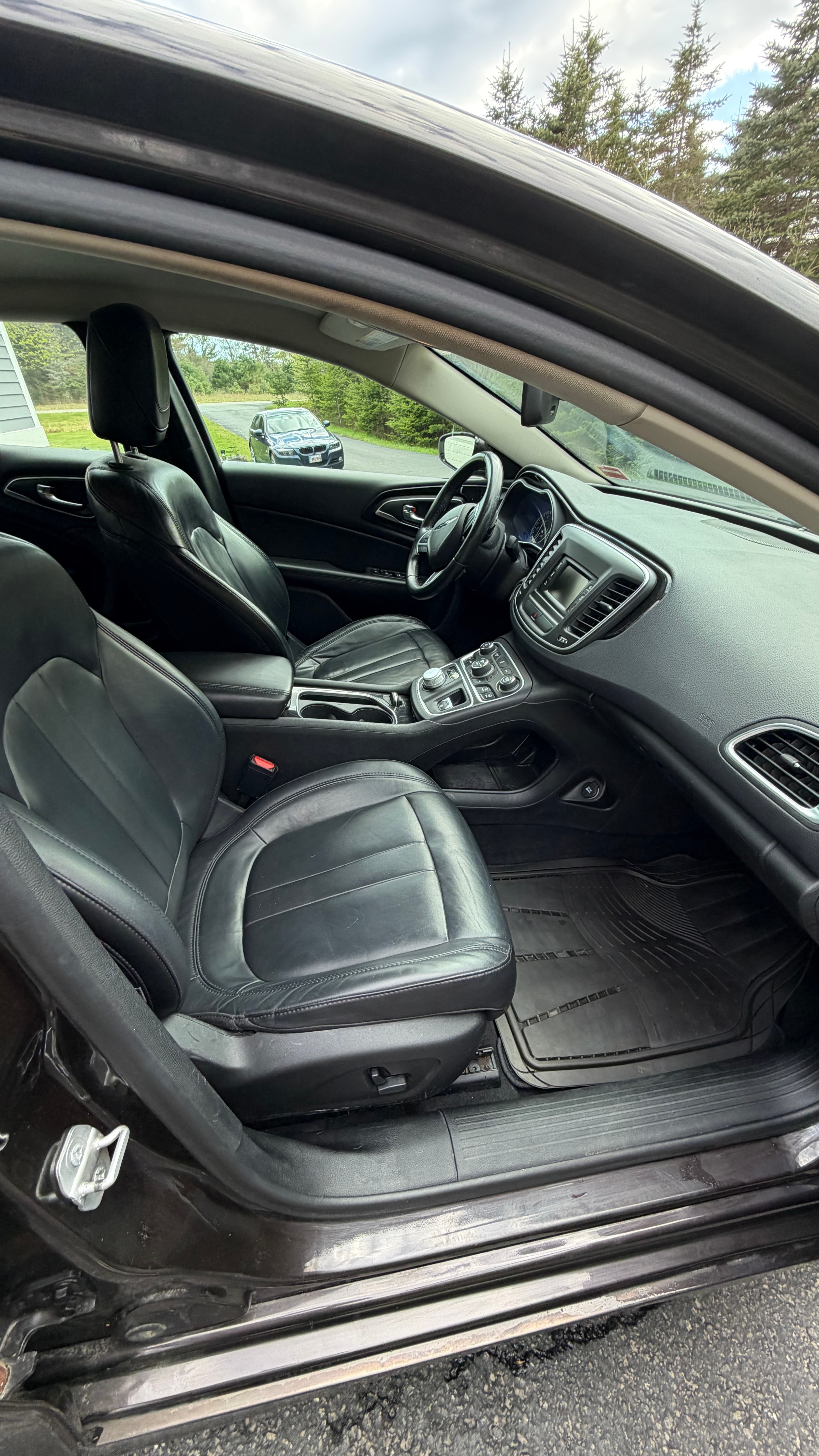 Front interior of a car with black leather seats, a dashboard, and a steering wheel.
